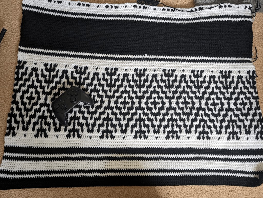 The  updated progress on my mosaic crochet blanket with a nintendo controller for scale
